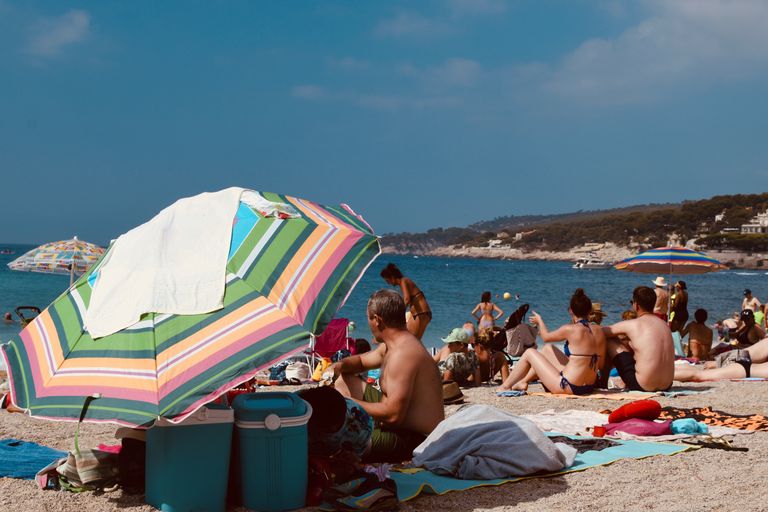 People enjoying a sunny day at the beach in Cassis, France under colorful umbrellas.